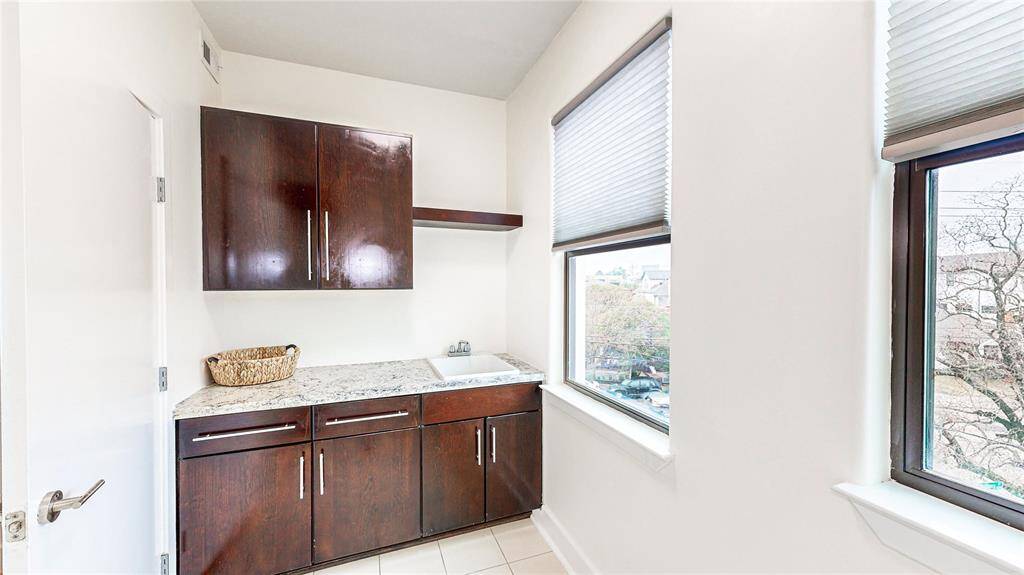 This photo shows a bright utility room with modern dark wood cabinets, a sink, and large windows that provide ample natural light. The space is clean and functional, ideal for laundry or storage.