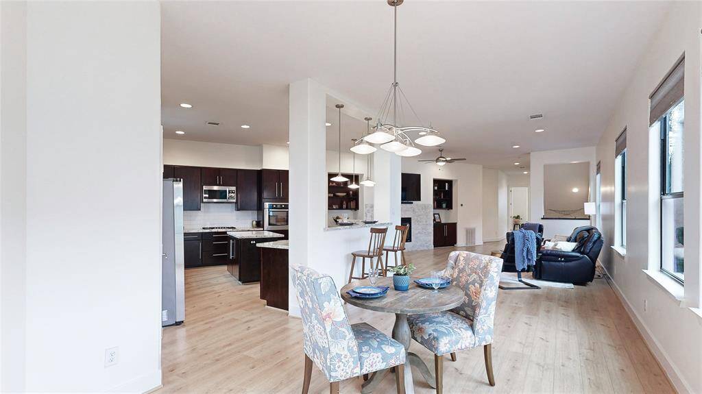 This photo showcases a modern open-concept living space with a bright and airy feel. The living area is visible in the background, offering ample natural light from large windows. The wood-look floors add warmth throughout the space.