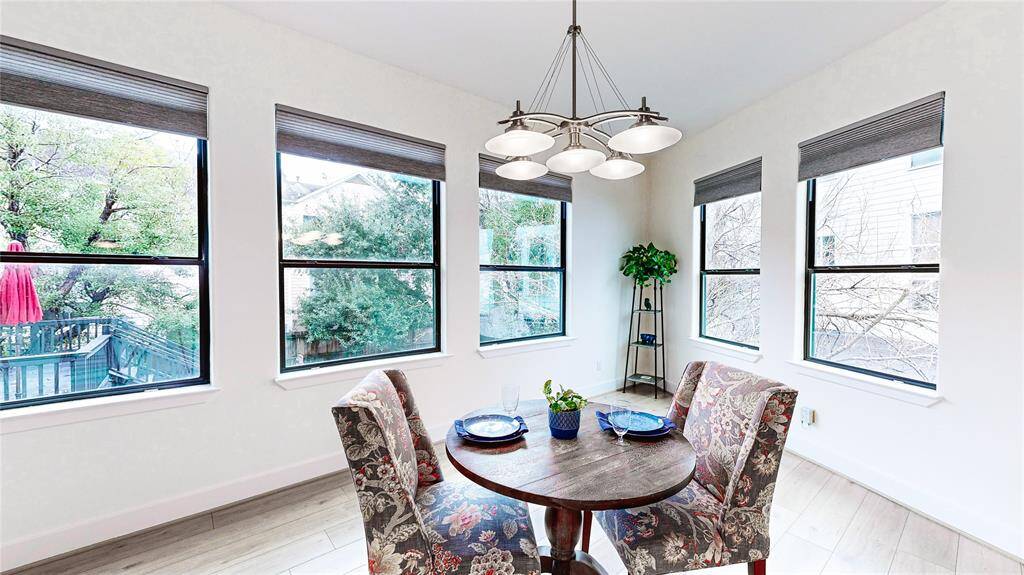 This bright dining area features large windows with views of greenery, and a stylish overhead light fixture, creating an inviting, airy space perfect for meals.