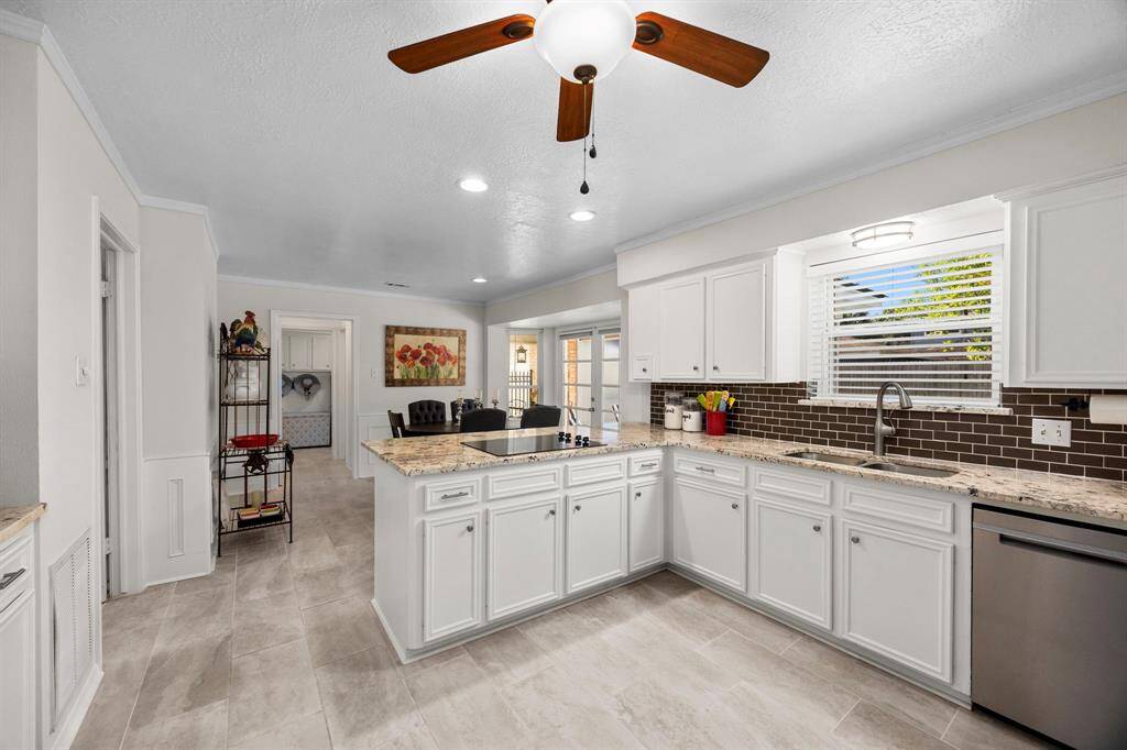 Spacious kitchen shows off granite counters and decorator backsplash, black electric cooktop, stainless sink and dishwasher.