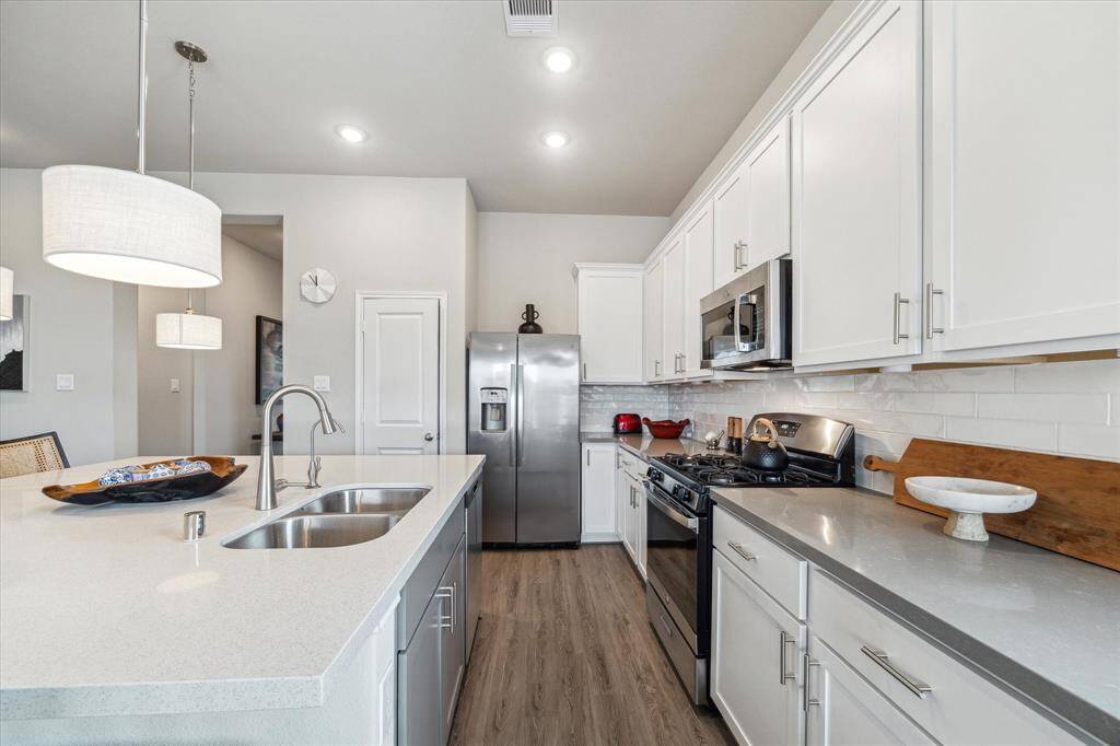 The heart of the home shines in this open-concept kitchen, featuring crisp white cabinetry, subway tile backsplash, OmegaStone countertops, stainless steel appliances, under-cabinet lighting, and a walk-in pantry.