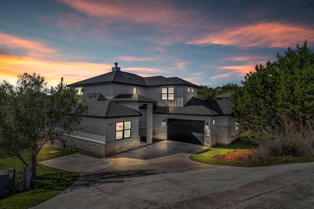This modern two-story home features a sleek design with a combination of stone and siding exterior. It includes a spacious driveway, a two-car garage, and is surrounded by lush greenery. The sunset backdrop enhances its curb appeal.