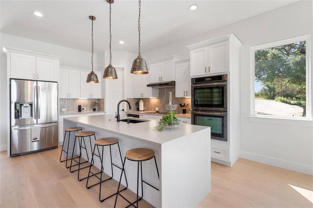 Modern kitchen with a spacious island featuring seating for four. It includes stainless steel appliances, white cabinetry, and pendant lighting, offering a bright and inviting space with large windows that present beautiful views of the lake.