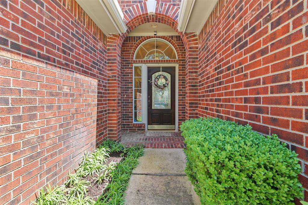 View of the front entry of home with landscaping and brick surround.