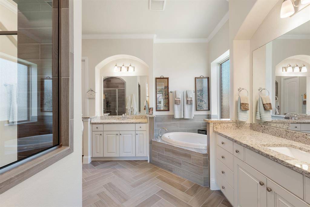 Wow!! Look at this Primary bathroom. Dual sinks separated by this large soaking tub and beautiful archways over the sinks, wood-look tile flooring, and a large shower (to the left).