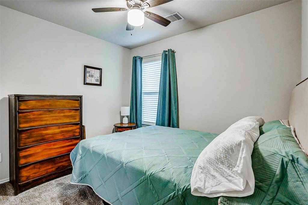 This secondary bedroom features plush carpeting for added comfort, a window that fills the space with natural light, and a high ceiling with a ceiling fan for year-round comfort.