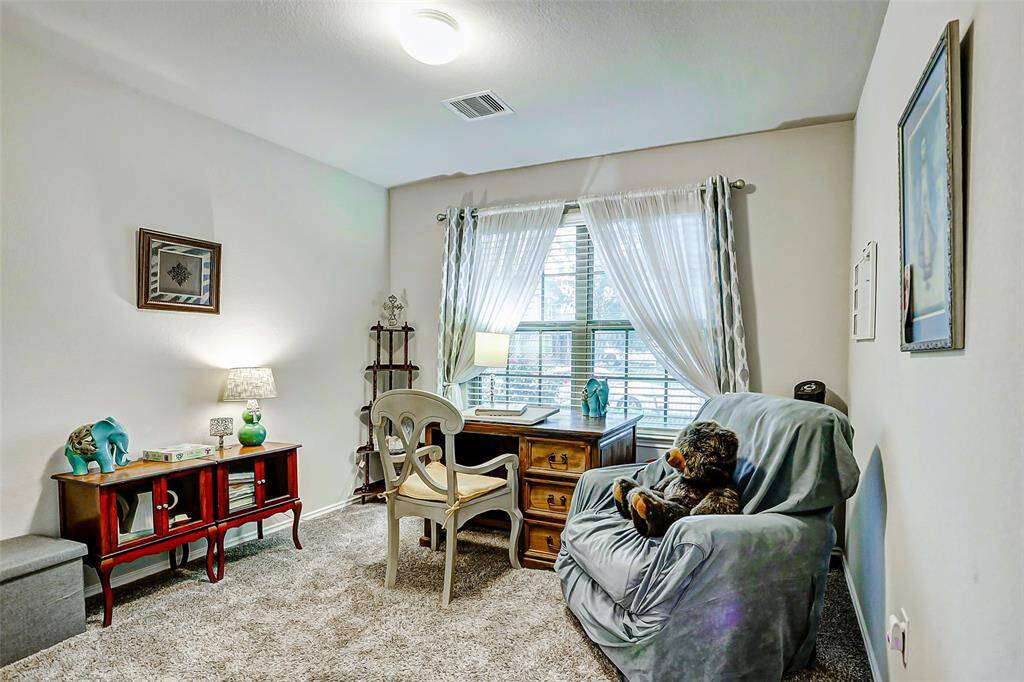 This secondary bedroom features plush carpeting for added comfort, a large window that fills the space with natural light, and a high ceiling.
