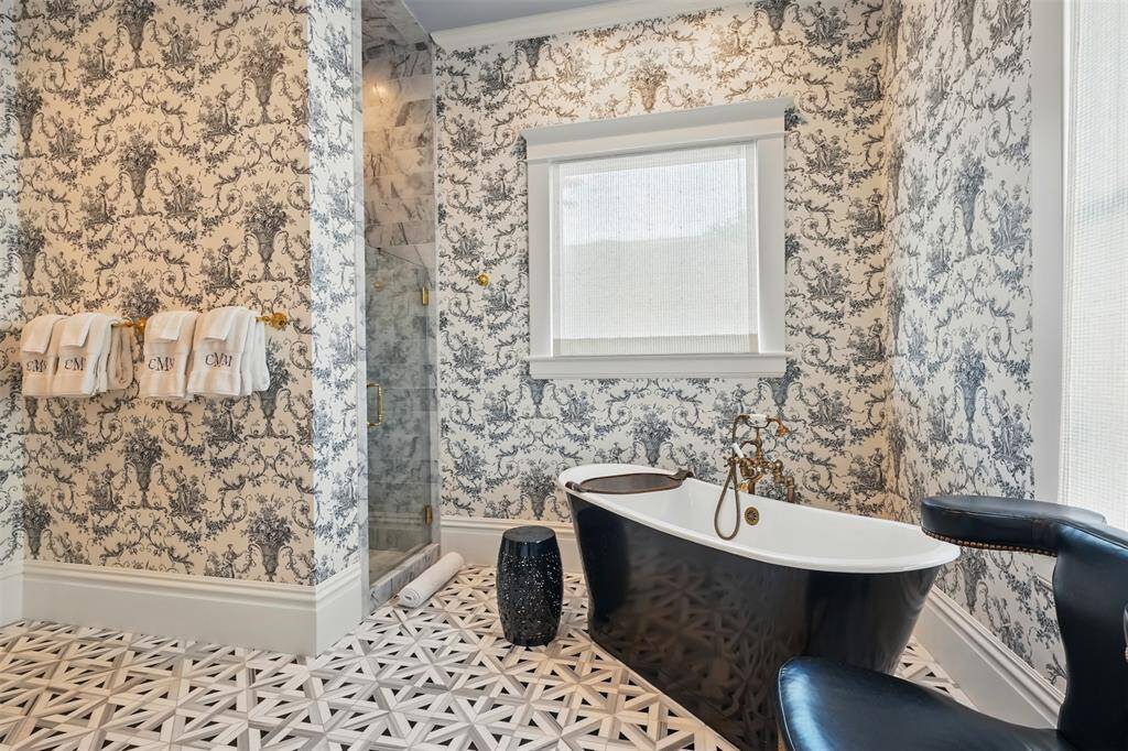 Timeless elegance meets thoughtful craftsmanship in the primary bath—a serene sanctuary of refined indulgence. A sculptural pedestal soaking tub with brass fixtures invites relaxation, while the marble-lined shower, enclosed in frameless glass, delivers modern functionality without compromising on style.
