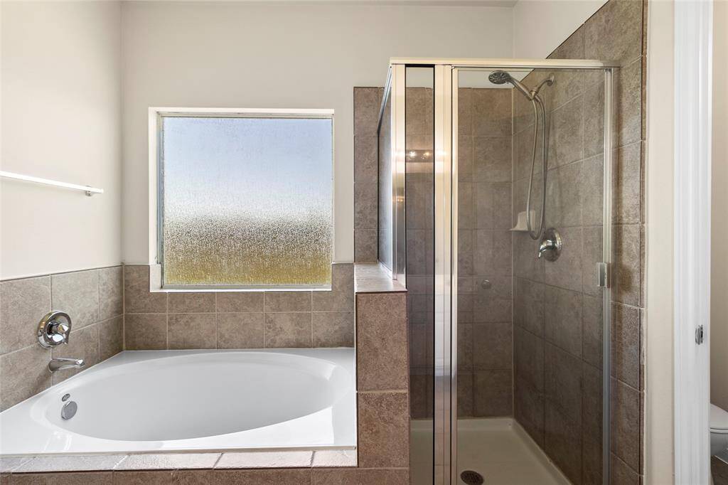 Indulge in your private en-suite featuring a spacious soaking tub and separate walk-in shower, perfectly framed by a frosted window that brings in natural light while maintaining privacy—your personal retreat to recharge in peace.