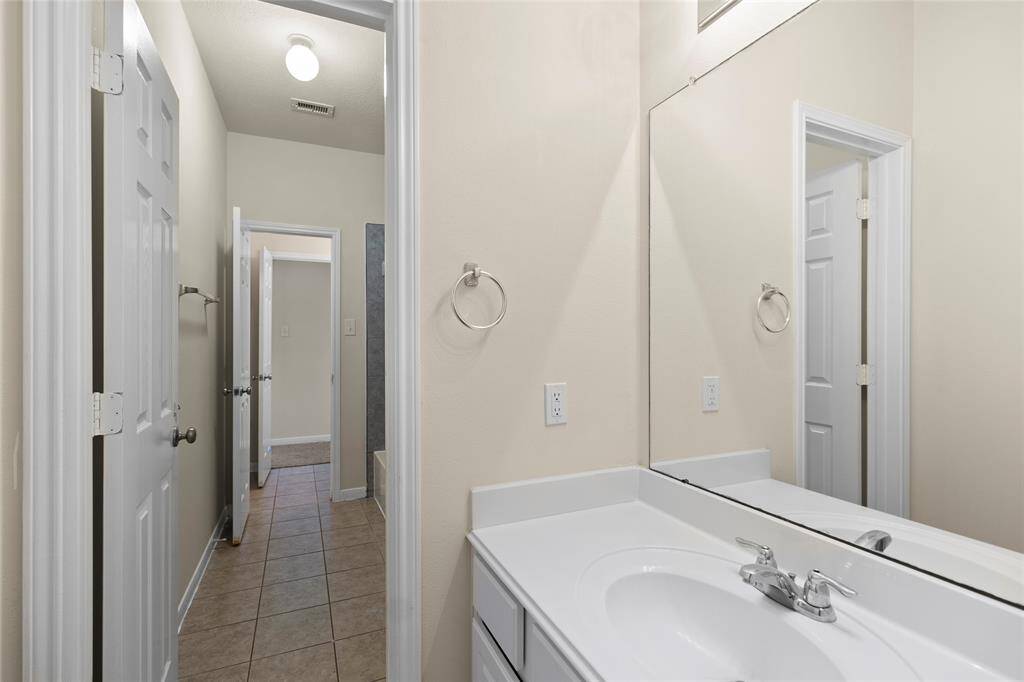 This full bathroom features a clean layout with a single-sink vanity, a large mirror, and neutral tile flooring. Dual entry doors connect to both sides of your home, offering a convenient setup for shared use or easy guest access without sacrificing privacy.
