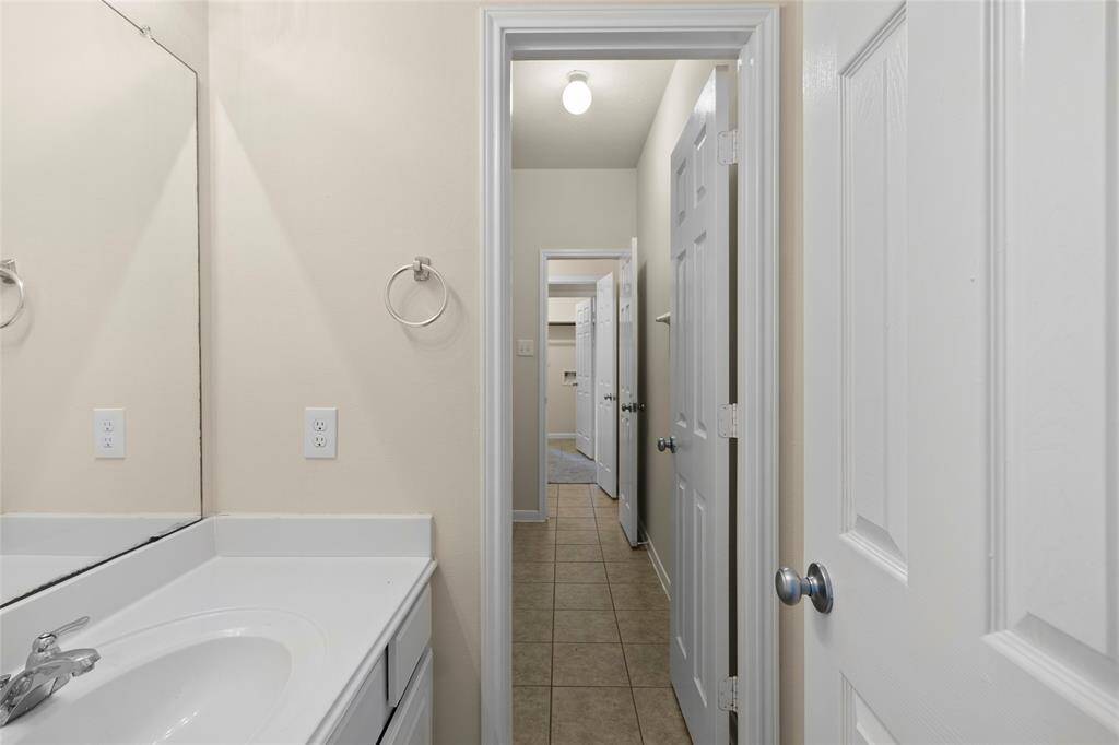 Step into a bathroom that maximizes space and function, with a long hallway-style layout that connects seamlessly to other areas of the home. A large mirror, crisp white vanity, and neutral finishes give it a fresh, clean feel—perfect for daily routines or accommodating guests.