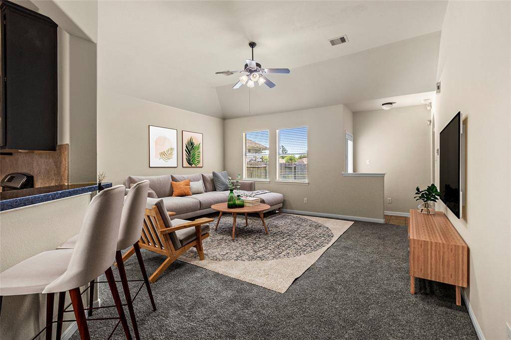 The spacious living area offers comfort and versatility with its soft carpeting, vaulted ceiling, and large windows that fill the space with natural light. The open layout flows seamlessly from the kitchen, creating an ideal setup for both relaxed evenings and entertaining guests. A ceiling fan adds a practical touch, while backyard views bring in a serene vibe—perfect for making this space truly your element.