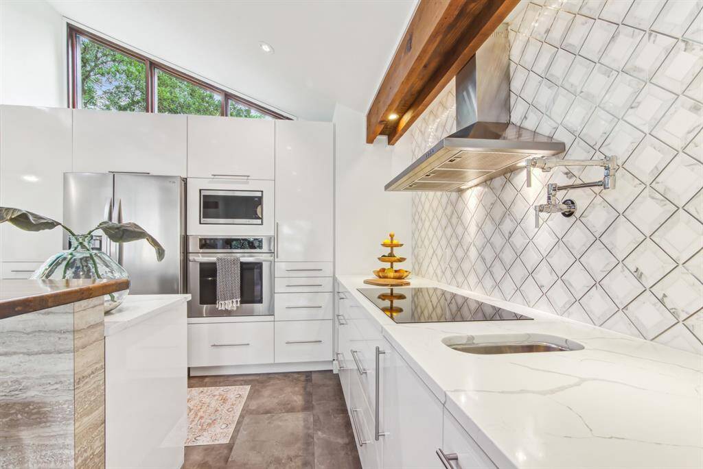 Additional sink with filtered water. view of the quartz counter top with elegant tile back splash and induction cook top.