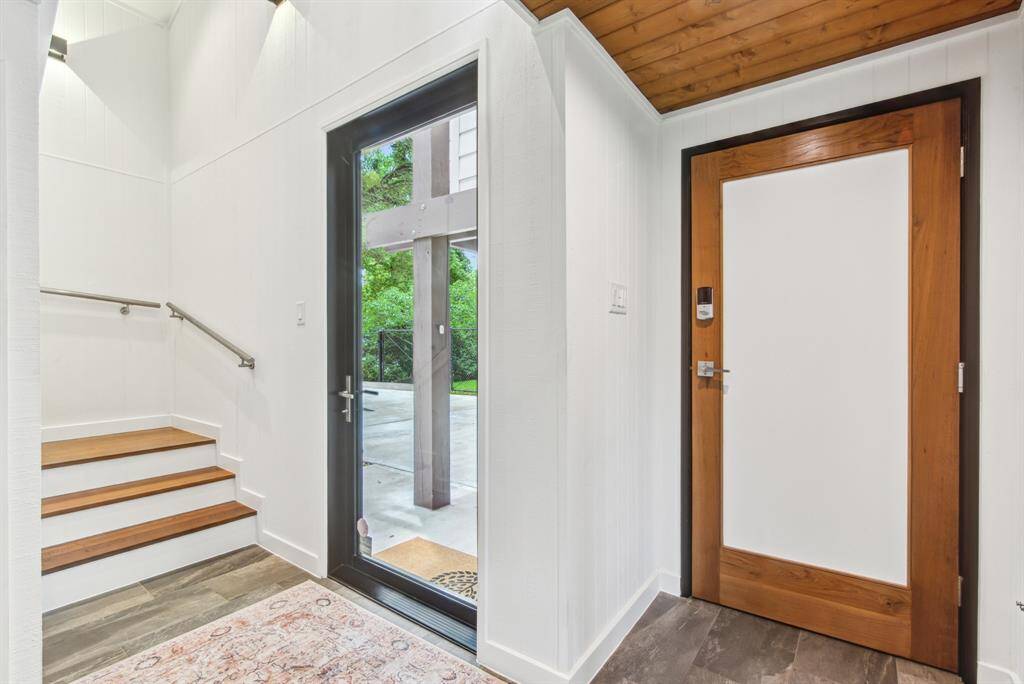 Vaulted ceiling entryway with hurricane certified front door. Teak door to garage and steps to living space.