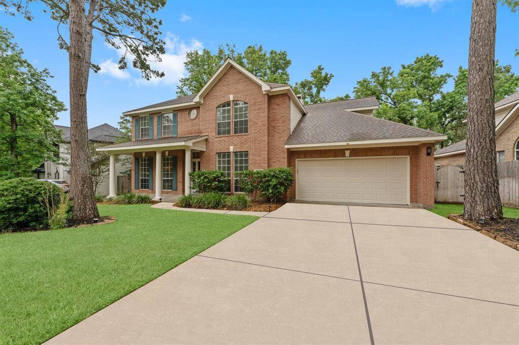 Charming two-story brick home with a welcoming front porch, nestled among mature trees. Features three-car tandem garage and a well-maintained lawn, creating a serene suburban feel.