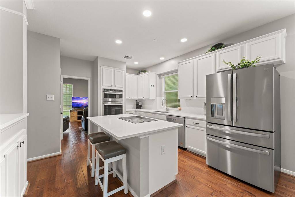 This modern kitchen features sleek white cabinetry, stainless steel appliances, and a central island with seating. Hardwood floors and recessed lighting add warmth and brightness, creating a welcoming space for cooking and entertaining.