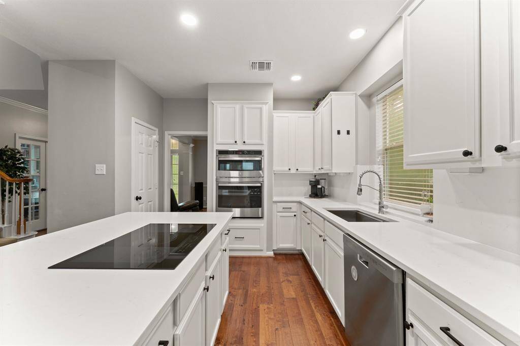 This kitchen features sleek white cabinetry, modern appliances, and an island with an electric cooktop. It has wood flooring, recessed lighting, and ample counter space, creating a bright and functional cooking area.