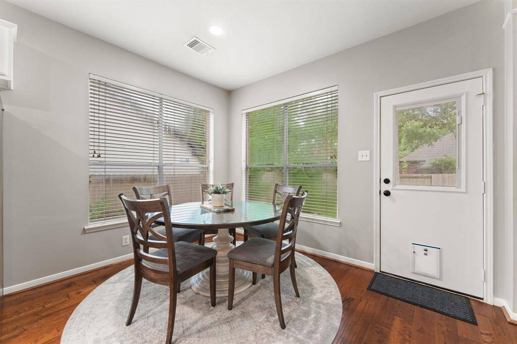 Bright dining area with large windows, hardwood floors, and a cozy round table for four. The space includes a door with a pet flap, offering easy access to the backyard.