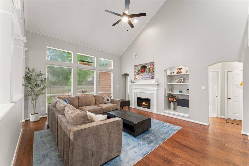 Spacious living room with high vaulted ceilings, large windows, and abundant natural light. Features a cozy fireplace, built-in shelves, and hardwood floors. Ideal for relaxation and entertaining.