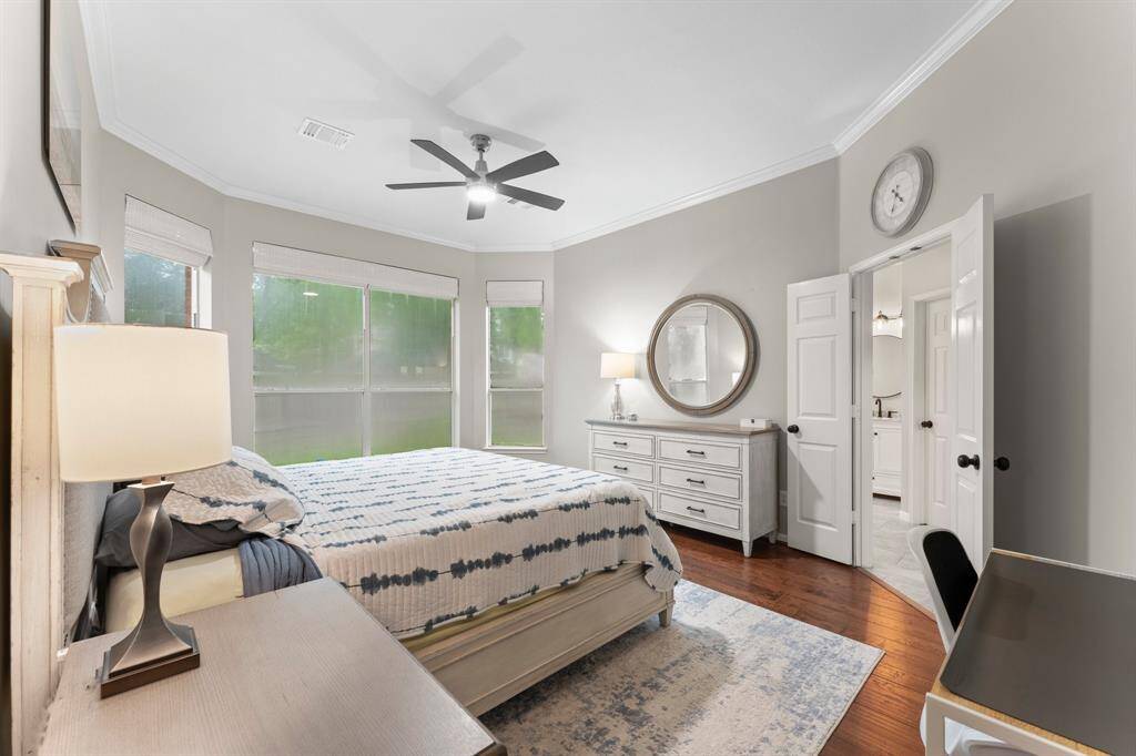 This primary bedroom features large windows providing ample natural light, elegant hardwood floors, and a soothing neutral color palette. It includes a stylish ceiling fan and access to an adjoining bathroom. Perfect for a cozy and inviting atmosphere.