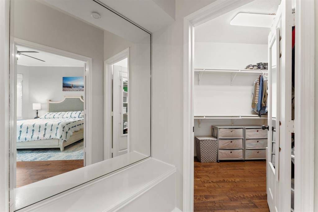 This photo shows a view from a bedroom into a spacious walk-in closet. The bedroom features a neatly made bed with a blue and white color scheme, while the closet offers ample storage with shelves and drawers. The hardwood floors add warmth to the space.
