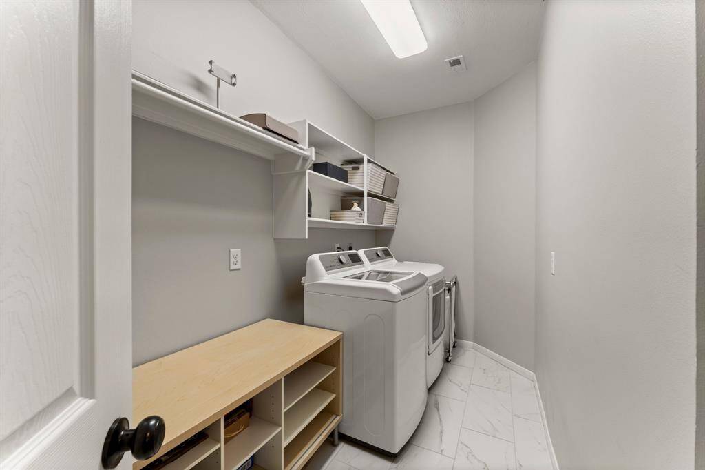 This photo shows a modern laundry room with a washer and dryer. It features clean white walls, a tiled floor, and ample shelving for storage.