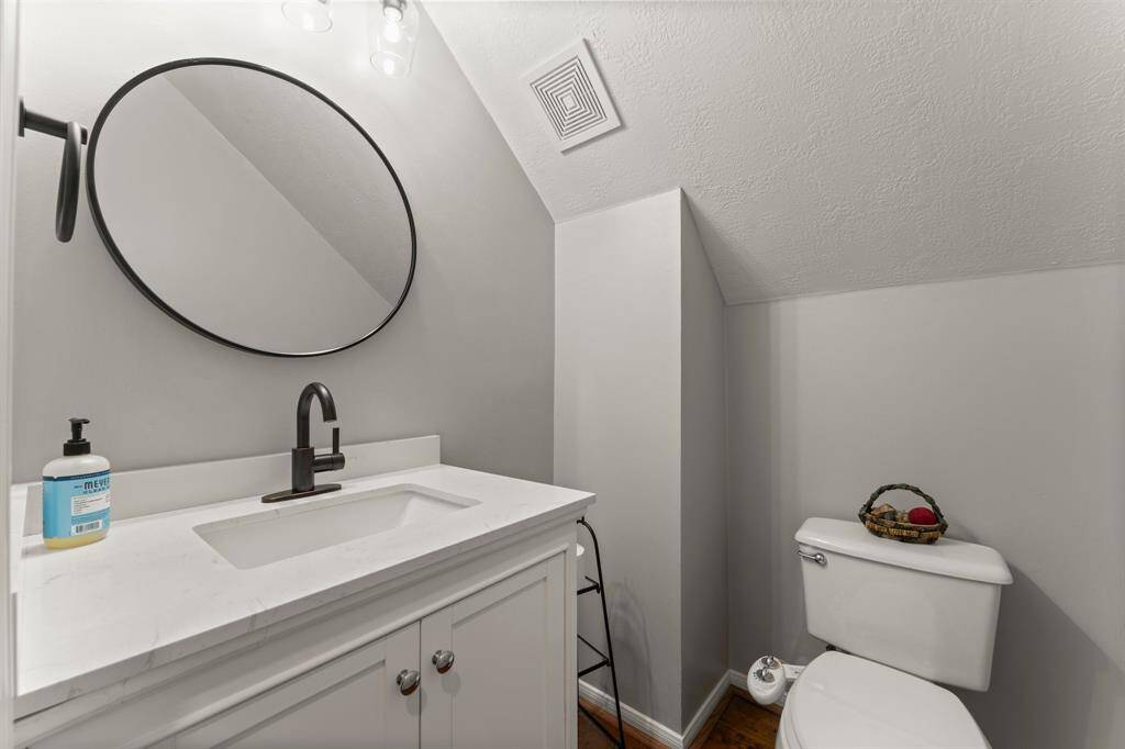 This photo showcases a modern bathroom with a sleek white vanity, a black faucet, and a round mirror. The space features a compact design, with neutral walls and a sloped ceiling.