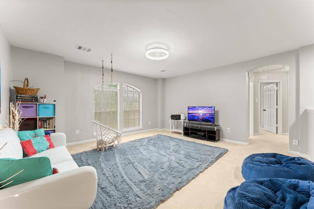 This spacious, light-filled room features neutral walls, a soft carpet, and large arched windows. Creating an inviting space perfect for relaxation or family gatherings.