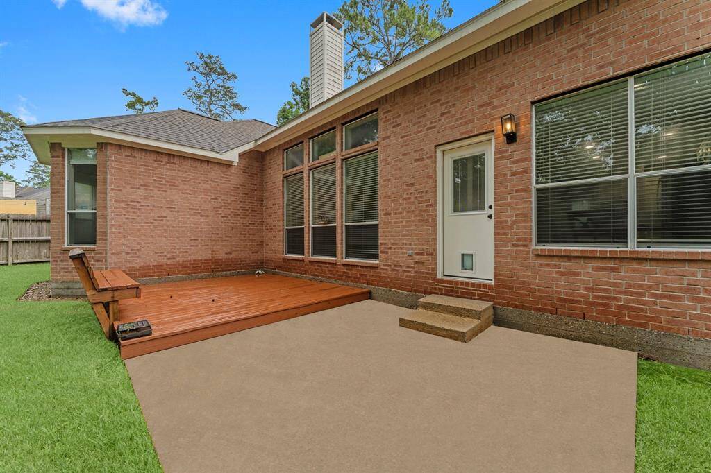 This photo showcases a brick exterior of a home with a cozy patio area, featuring a wooden deck and a small step leading to a door with large windows. The yard is grassy and fenced, providing a private outdoor space.