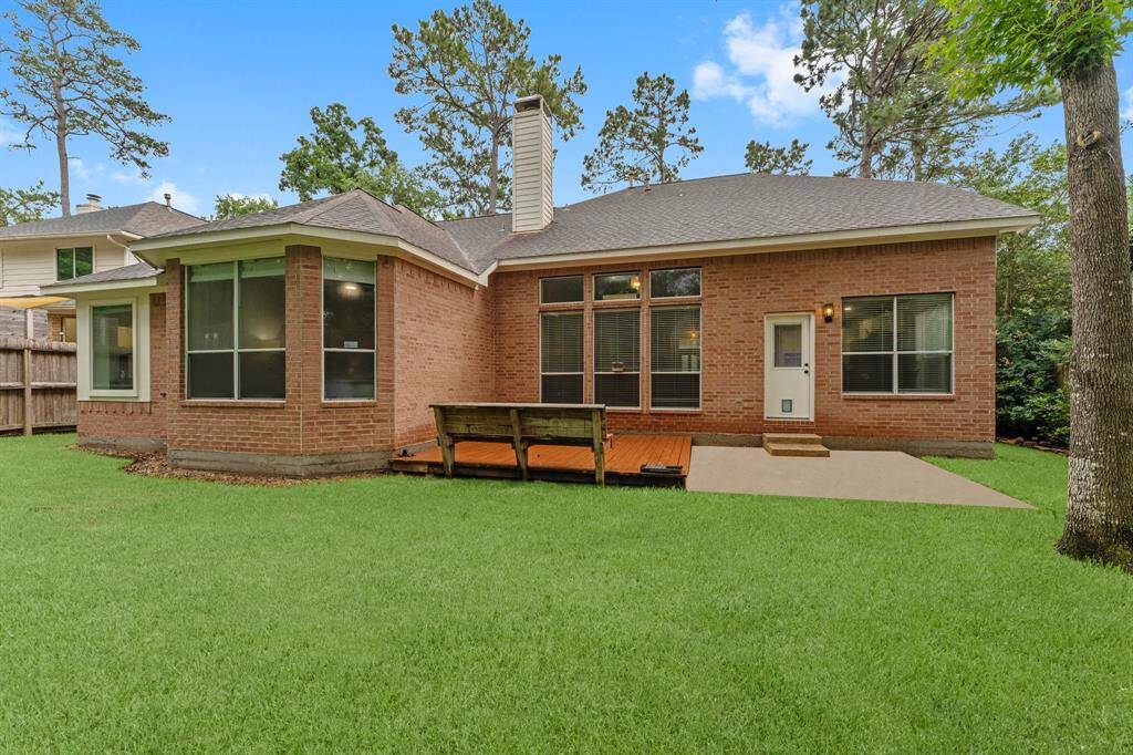 This photo depicts a charming brick home with a spacious backyard. It features large windows for ample natural light and a cozy wooden deck, perfect for outdoor relaxation. The surrounding mature trees add privacy and a touch of nature.