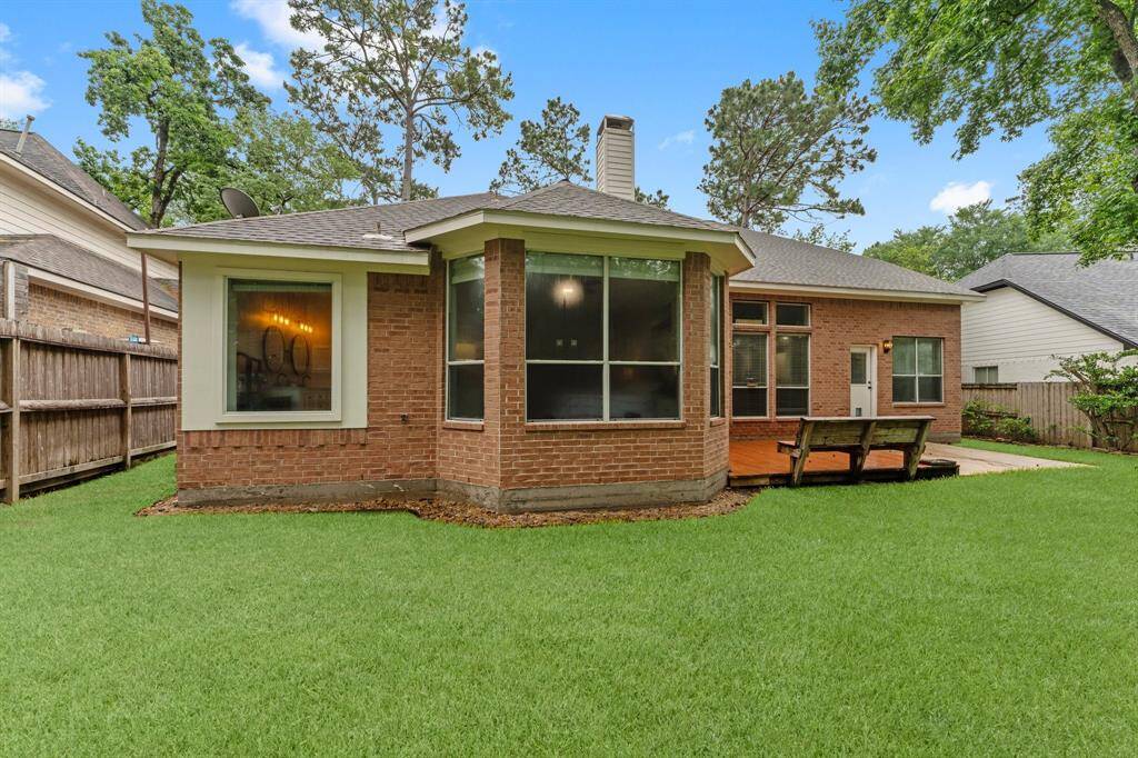 This photo showcases the backyard of a brick home featuring a well-maintained lawn, a wooden deck area, and a fenced perimeter. The house has large windows for ample natural light, and mature trees provide a sense of privacy and greenery.