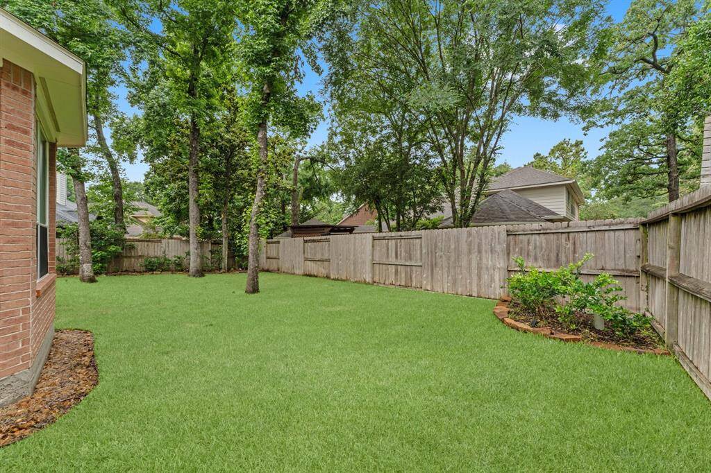 This photo shows a spacious, fenced backyard with lush green grass and mature trees, providing a private and serene outdoor space.