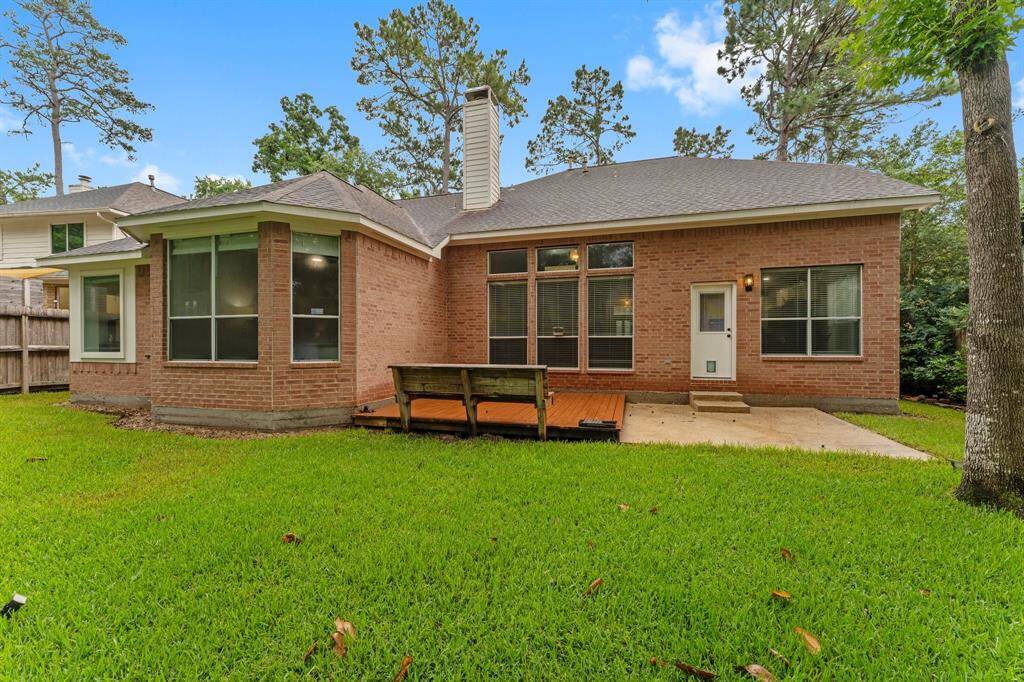 This photo showcases a single-story brick home with a spacious backyard. It features large windows for ample natural light, a small wooden deck, and a well-maintained lawn surrounded by mature trees, providing a serene outdoor space.