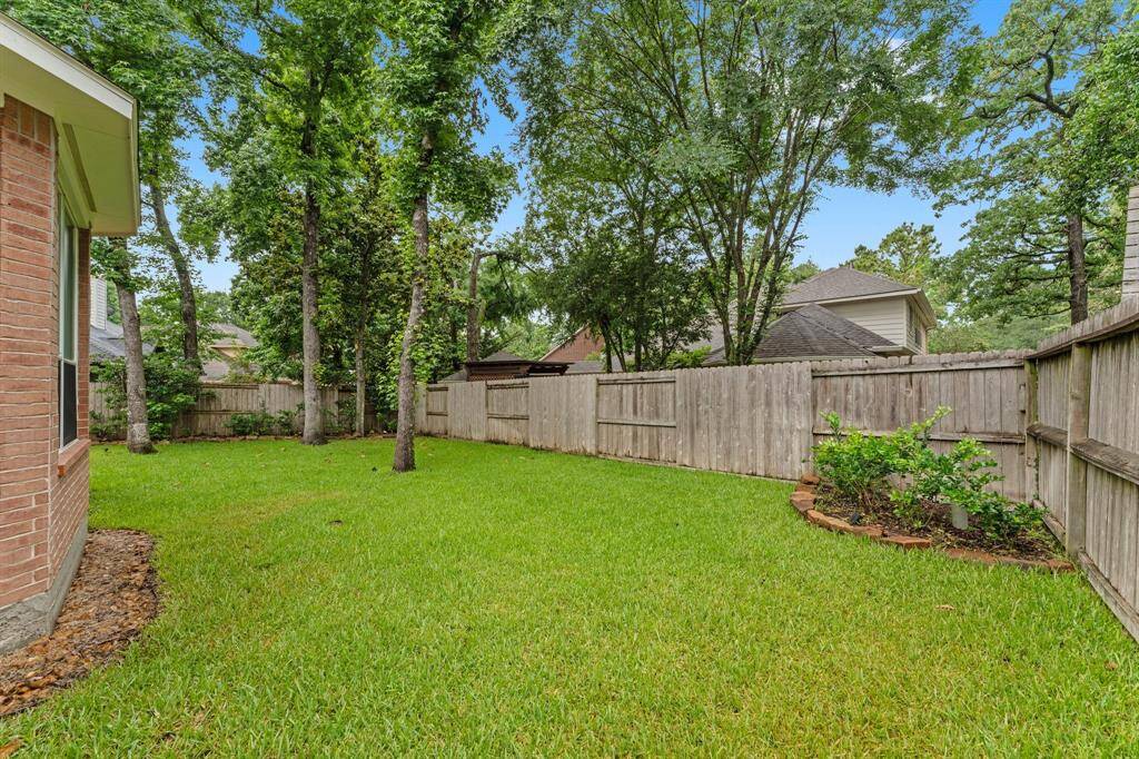 This photo shows a spacious backyard with lush green grass, mature trees, and a wooden privacy fence, ideal for outdoor activities and relaxation.