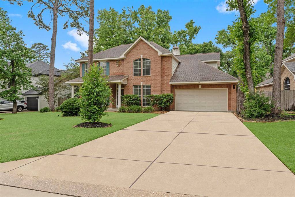 This photo showcases a charming two-story brick home with a well-maintained front yard, spacious driveway, and attached three-car garage. The property is surrounded by mature trees, adding a sense of privacy and natural beauty.