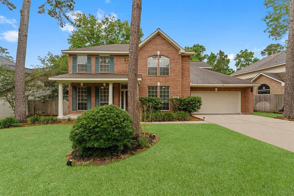 Charming two-story brick home with a welcoming front porch, set amidst mature trees. It features a well-maintained lawn, a two-car garage, and a spacious driveway. Ideal for family living with a classic, inviting exterior.