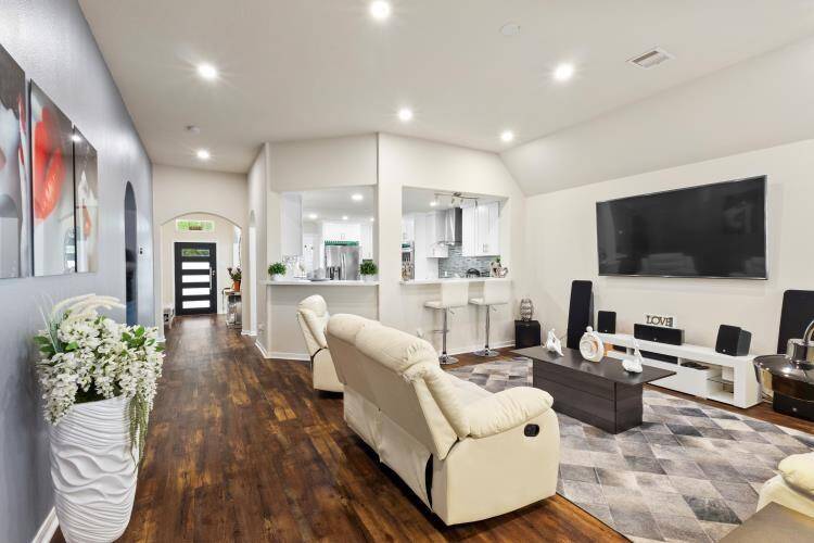 This inviting family room features an open layout with elegant hardwood floors, modern recessed lighting, and a seamless flow to the kitchen. Ideal for gatherings and relaxation, it offers ample space and contemporary style.