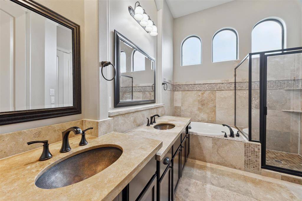 Primary bathroom featuring dual copper sinks, a glass-enclosed shower, a jetted tub, and arched windows that flood the room with natural light, creating a serene and luxurious atmosphere.