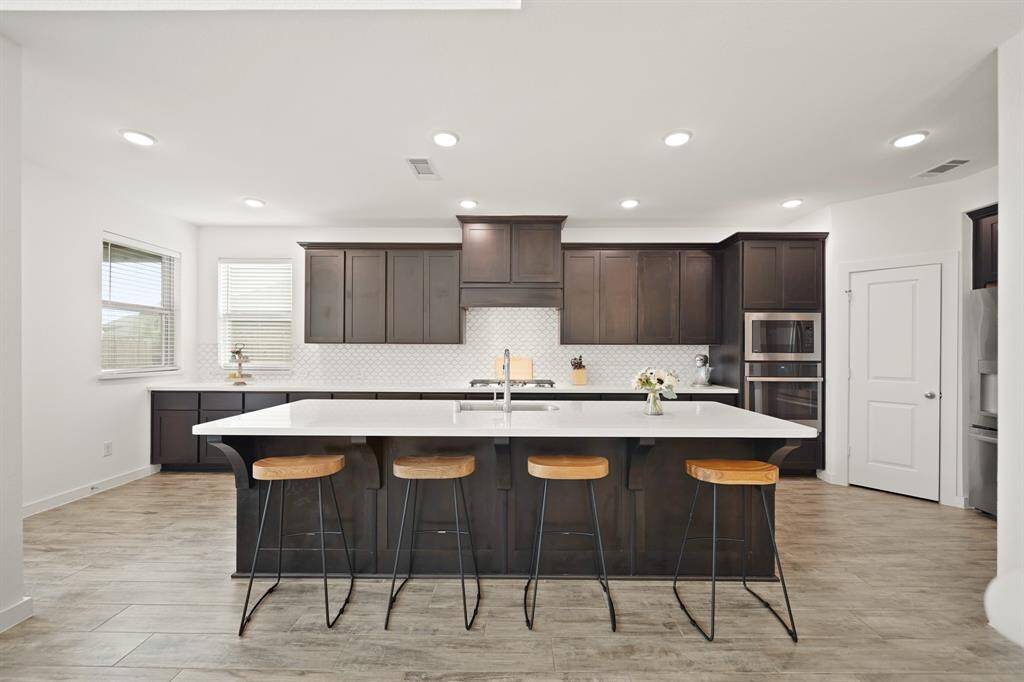This gourmet cook's kitchen with recessed lighting and tile flooring includes 42" wood-stained Shaker-style cabinets capped with crown moulding highlighted by a tiled back splash with quartz counter tops.