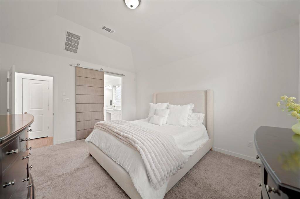 A view of the owner's bedroom with the private bath accessible through the sliding barn door entrance shown in the background.