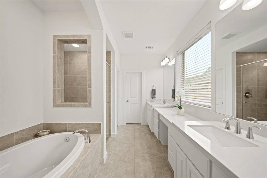 Luxuriously appointed, the private bath has dual dressing areas with painted cabinets supporting a quartz counter top with an integrated back splash, wall mounted mirrors & lighting above separated by a make-up vanity area & tile flooring.