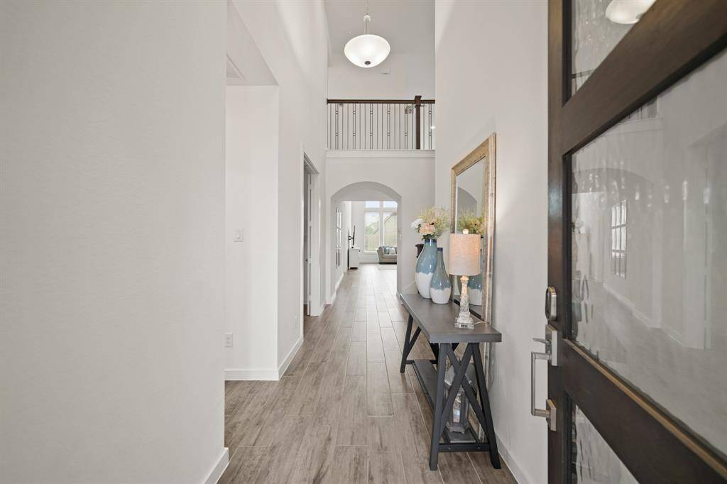 The foyer of the home with a soaring ceiling and balcony views from above includes recessed and pendant chandelier lighting, space for accent furniture and hardwood tile flooring.