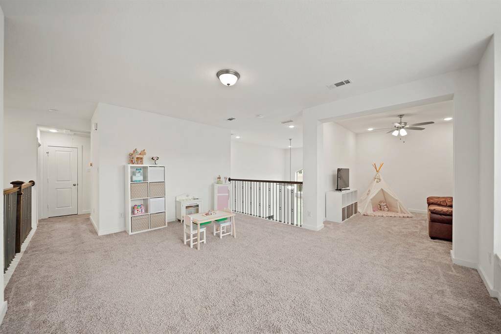 The second floor game room with wrought iron balconies offering views of the foyer & living room below includes ceiling mounted lighting & carpet.
