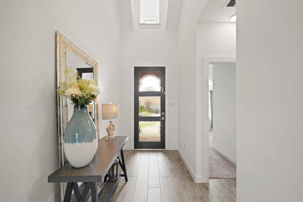 Included is a wood-stained front door with privacy glass and keyless entry. Nearby is spacious under-stair coat/storage closet and a secondary, first floor bedroom with access to a full bath is accessible on the right.