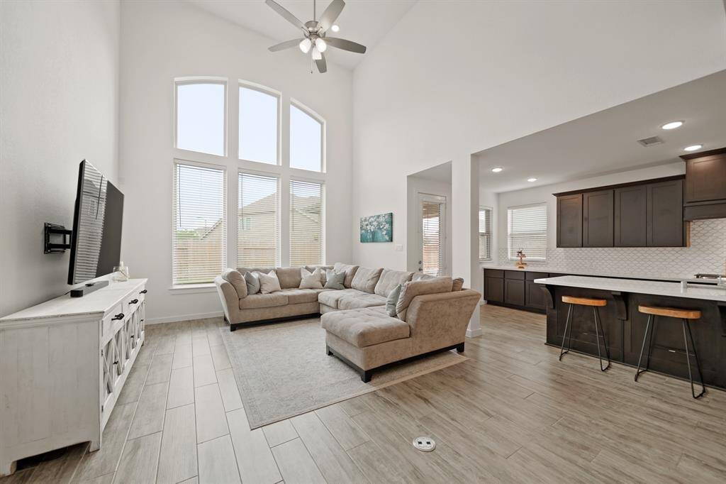 The living room has a two-story ceiling with recessed lighting, ceiling fan with light fixture & hardwood tile floors.