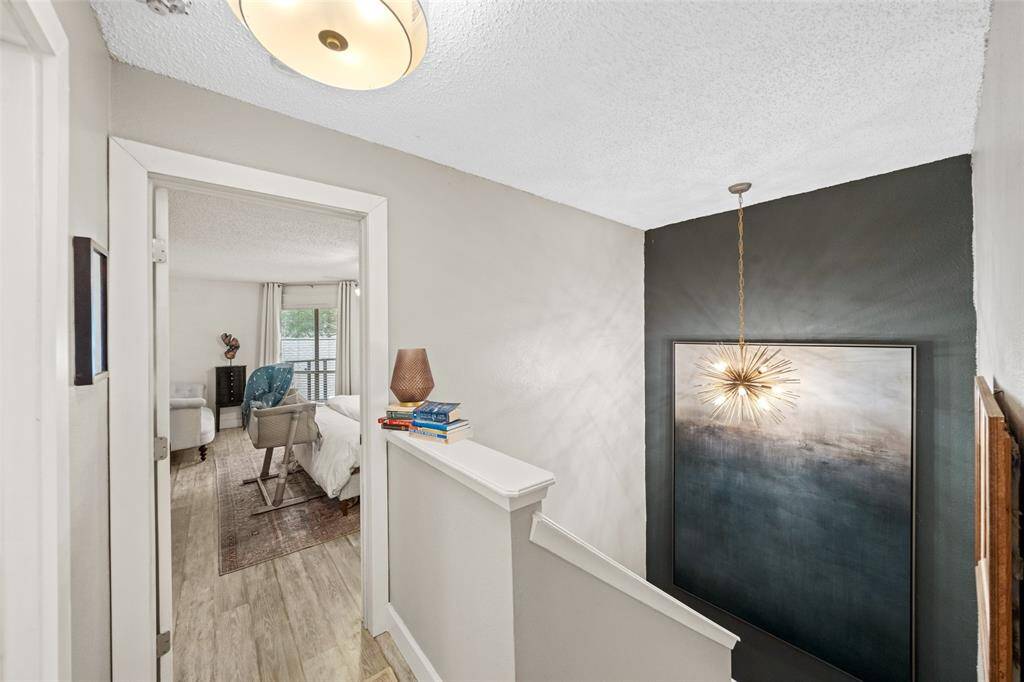 This hallway features a modern light fixture, textured walls, and leads into a bright bedroom with large windows. The space is well-lit and inviting.