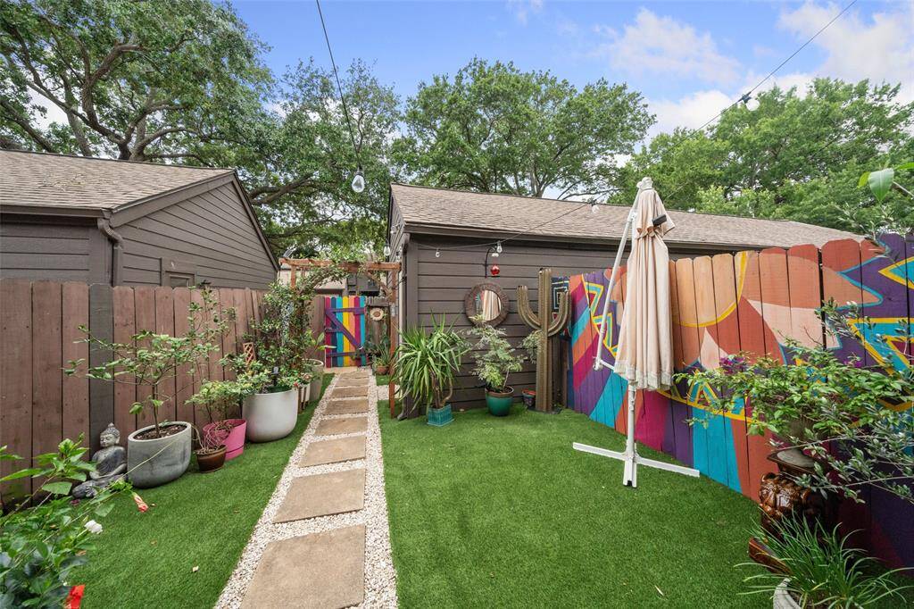 Charming backyard with artificial grass, vibrant murals on the fence,  The space features a stone walkway leading to a gate, creating a cozy and colorful outdoor retreat.