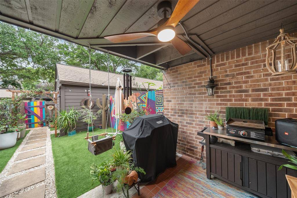 This cozy outdoor space features a covered patio with a ceiling fan. Backyard includes a mix of brick and wood elements,  lush greenery,  making it perfect for relaxation and entertaining.