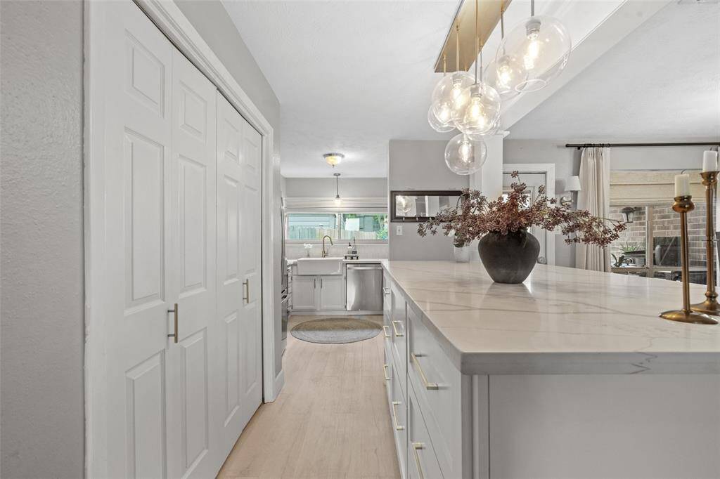 This photo showcases a bright, modern kitchen with a spacious island featuring beautiful countertops and pendant lighting. It leads to a cozy dining area with large windows, offering a seamless and inviting space for cooking and entertaining .