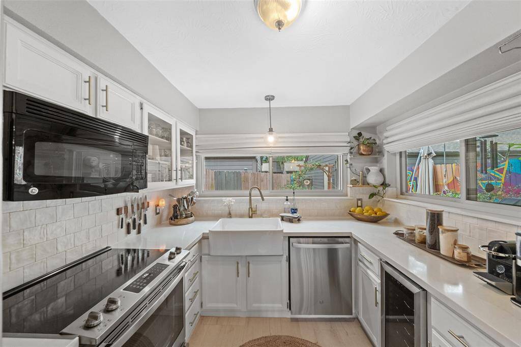 This kitchen is bright and modern, featuring white cabinetry, and a farmhouse sink. Large windows provide ample natural light and a view of the backyard. The space is efficiently designed with a stylish backsplash and sleek countertops.